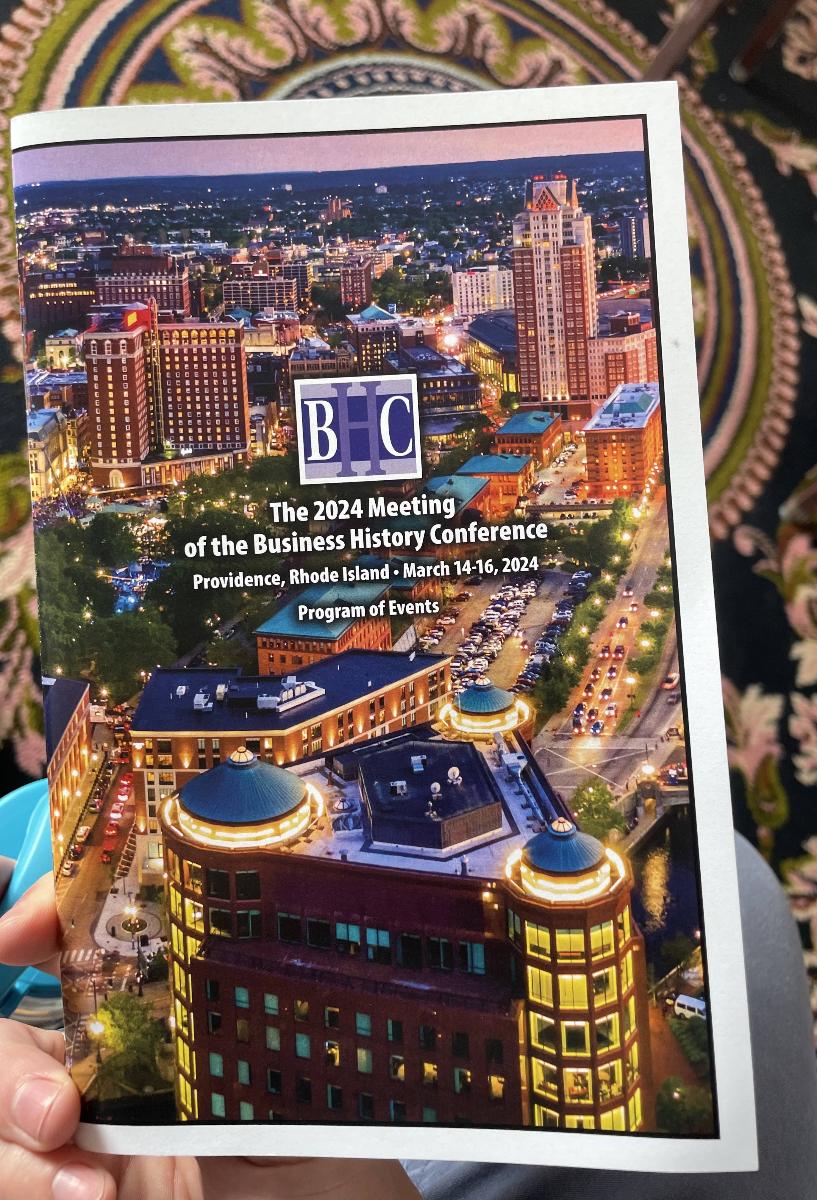 Photo of Kenaston holding the program for the Business History Conference. The program's background is a photograph of downtown Providence.