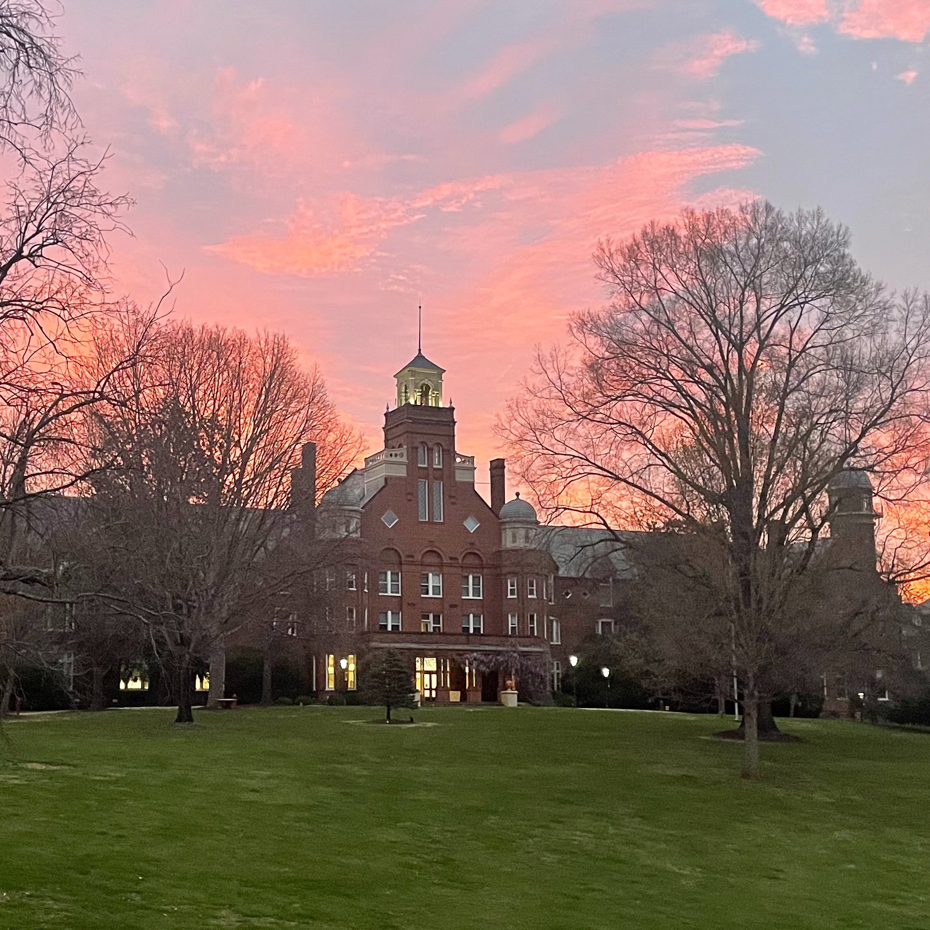 Sunrise of Randolph College's red-brick Main Hall. The sky is light pink and blue.